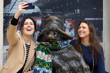 EDITORIAL USE ONLY left-right Lucia Cappiello and Grace Armitage take a selfie with the Paddington Bear statue at Paddington station, London. Paddington is wearing a bespoke Irish themed scarf from Tourism Ireland, to celebrate St Patrick’s Day. Picture date: Thursday March 14, 2024. PA Photo. Over 180,000 people are set to fly in from Great Britain to Ireland over St Patrick’s weekend. Flights to Ireland from Heathrow Airport ahead of St Patrick’s Day are accessible via the Heathrow Express and Elizabeth line, which both depart from Paddington Station.