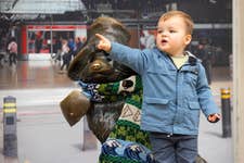 EDITORIAL USE ONLY William Jefferies aged 2 interacts with the Paddington Bear statue at Paddington station, London. Paddington is wearing a bespoke Irish themed scarf from Tourism Ireland, to celebrate St Patrick’s Day. Picture date: Thursday March 14, 2024. PA Photo. Over 180,000 people are set to fly in from Great Britain to Ireland over St Patrick’s weekend. Flights to Ireland from Heathrow Airport ahead of St Patrick’s Day are accessible via the Heathrow Express and Elizabeth line, which both depart from Paddington Station.