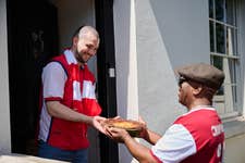 EDITORIAL USE ONLY Ian Wright lookalike, Rudy Brathwaite (right), delivers HelloFresh’s ‘Winner, Winner, Chicken (Pie) Dinner’ pie to Arsenal supporter Phil Mason at their home in London. Picture date: Tuesday May 26, 2026. PA Photo. Inspired by the former Arsenal footballer’s fondness for chicken pies, the dish has been reintroduced and renamed by the brand to mark Arsenal F.C.’s Premier League title win.
